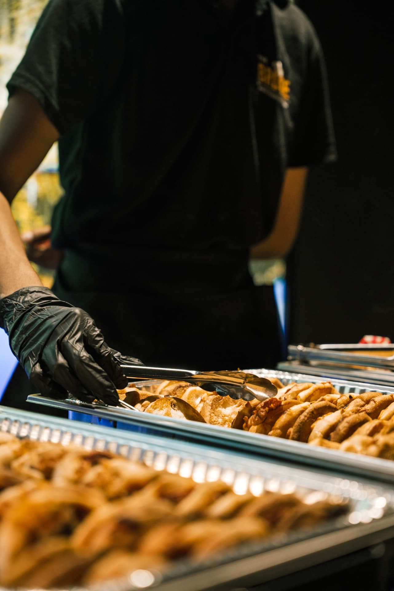 A gloved BRDGE team member serving pastries with tongs from a chafing dish